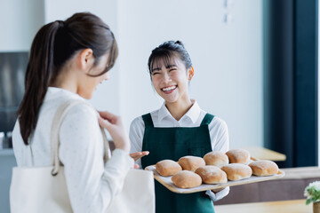 パンをお客様にすすめるベーカリーカフェの若い女性の店員
