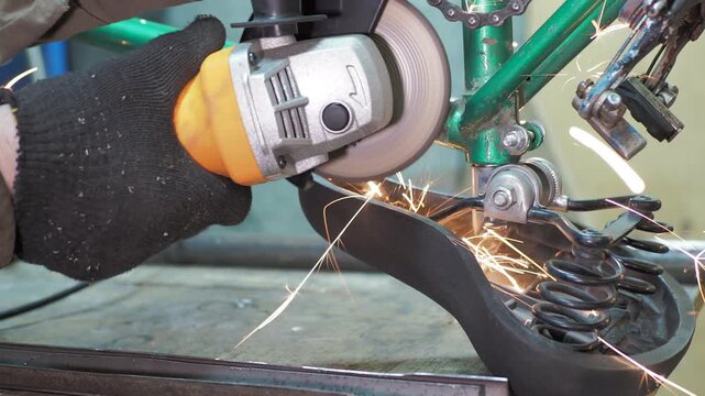 Workshop. A worker uses a angle grinder to grind the frame of an upside-down bicycle.