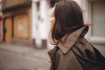Obraz premium Sensual young woman walk on the street, look elegant, close up portrait woman with hair under jacket, look calm, sensual. Woman wear green trench coat. Woman watch ahead, look by side.