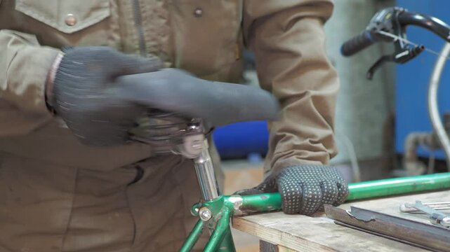 Workshop. A worker removes the seat from an old bicycle along with the seatpost.