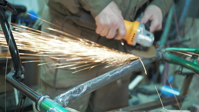 Workshop. A worker uses a angle grinder to grind the frame of an upside-down bicycle