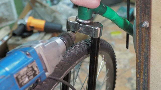Workshop. A worker uses a drill to make a hole in the steering fork of an old bicycle.