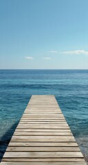 Naklejka premium Tranquil wooden pier stretches into a serene azure sea under a clear sky.