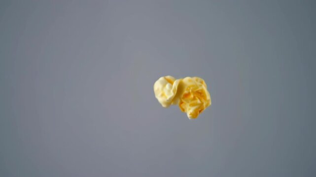 Single popcorn kernel in mid-air against a muted gray background