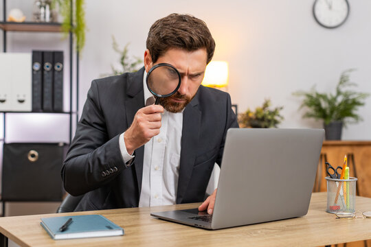 Middle-aged businessman at home office checks laptop screen with magnifier glass finds tiny font error. Freelancer guy at table verifies numbers notes issue and confirms audit result with relief ok. - Powered by Adobe