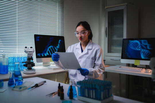 Female scientist in a lab coat and protective goggles is analyzing genetic codes and DNA structures on computer screens