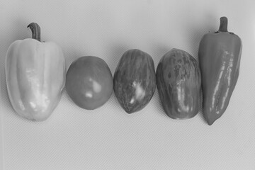 A clean, monochromatic overhead shot of a fresh vegetable assortment, including two bell peppers and three tomatoes, lined up on a textured white background.

