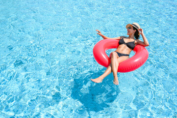 Young beautiful woman in bikini wear hat and sunglasses relaxing in swimming pool with rubber ring, Summer vacation concept.