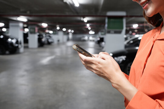 A woman is texting on her phone in a parking lot. The parking lot is empty, and the woman is smiling