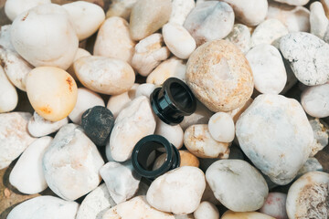 Black camera lens caps resting on smooth pebbles in natural outdoor setting with sunlight