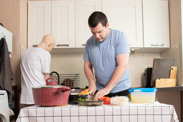Couple cooking healthy dinner together at home, man cutting vegetables and adding greens into bowl while woman in casual clothes watches thoughtfully, concept of family support and healthy lifestyle