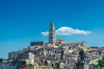 Obraz premium Vue du clocher de la Cathédrale de Matera et son quartier environnant sur fond de ciel bleu, avec un nuage derrière le clocher, Italie