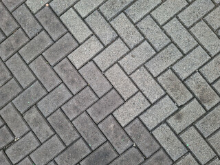 Close-up photo of paving block pattern arranged in a herringbone design. Road texture, floor surface, and urban architectural detail.