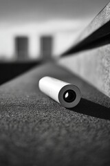A grayscale close-up of a cylindrical object, likely a portable audio device, resting on a textured surface.  Modern, minimalist aesthetic.  Architectural elements in the background