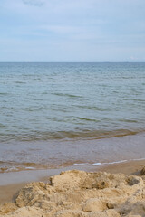 Minimalist landscape with light sand in the foreground, calm waves, and soft blue sky. The shot is wide with open copy space, natural colors, and serene mood. Copy space