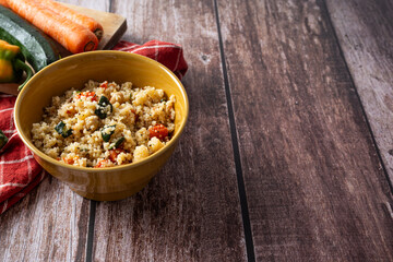 Rustic bowl of couscous with vegetables on dark wooden table