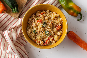 Bowl of cous cous with fresh vegetables on a white background.