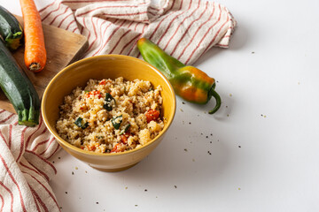 Bowl of cous cous with fresh vegetables on a white background.
