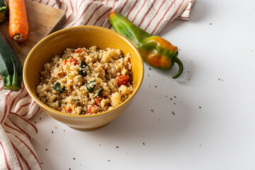 Bowl of cous cous with fresh vegetables on a white background.