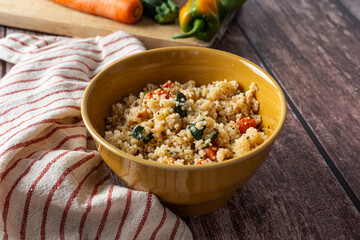 Rustic bowl of couscous with carrots, bell peppers, and zucchini on wooden table, styled with fresh vegetables. Ideal for concepts related to healthy eating, vegetarian diet, or Mediterranean cuisine.