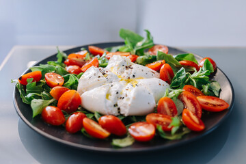 Fresh salad featuring creamy burrata cheese, vibrant cherry tomatoes, and mixed greens, beautifully arranged on a black plate, showcasing healthy and delicious culinary presentation
