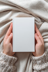 Gentle Hands Holding a Blank White Book on a Soft Beige Knitted Blanket, Simple Elegance