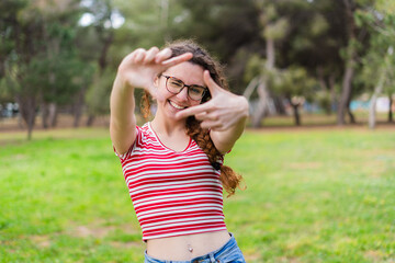 Obraz premium Smiling young woman making a frame with her fingers in a park