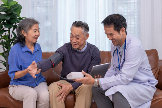 health visitor using tablet computer giving advice a senior woman for checking blood pressure her husband at home,concept for home health services,home care,self health care