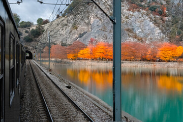Train passing along turquoise river with colorful autumn trees reflecting on the water.