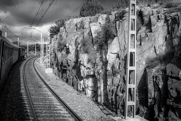 Black and white railway scene with train passing next to rugged rock cliffs.