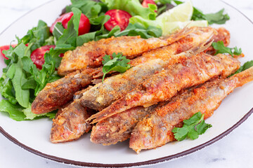 Fried crispy mullet fish, with fresh salad, on a plate with lime, no people,