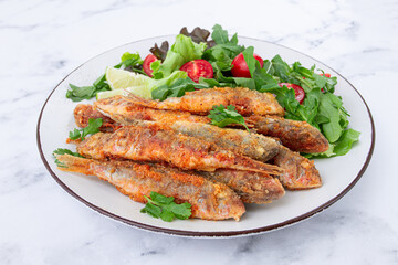 Fried crispy mullet fish, with fresh salad, on a plate with lime, no people,