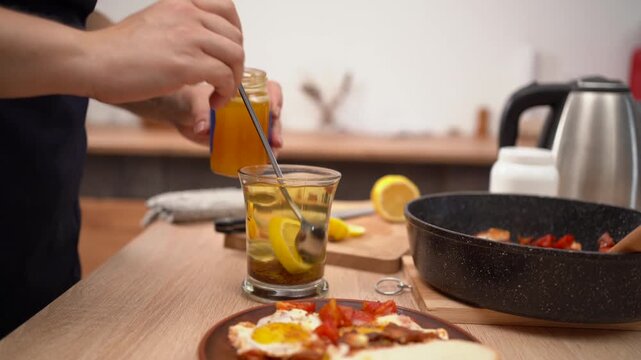 Woman cooking breakfast with fried eggs and hot tea with honey, lemon. Health concept.