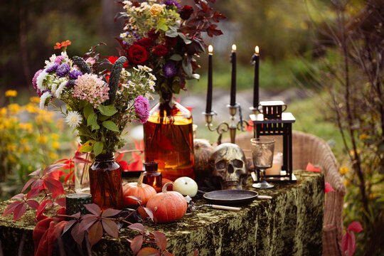 Fall themed holiday table setting arrangement for a seasonal party, glasses, pumpkins, candles, field flowers. Halloween table in the garden with scull, black candles and autumn flowers