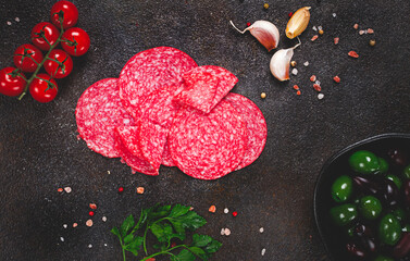 composition of sliced salami, with fresh tomatoes, garlic and green olives, on a dark surface, appetizer, no people,