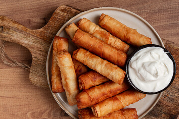 fried spring rolls with cheese, on a wooden background, with cream sauce, no people,