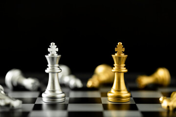 Golden and silver chess king pieces facing each other on a chessboard with fallen pieces, dark background.