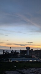 The sun sets over the ocean, casting a warm glow on the water tower and surrounding landscape, creating a serene and picturesque scene at dusk