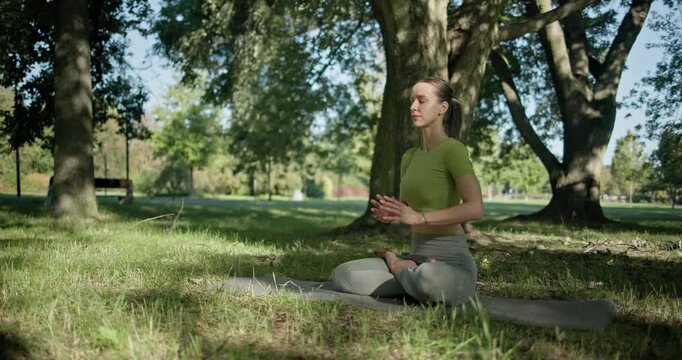 young beautiful white girl doing yoga in park among trees in clearing on summer day