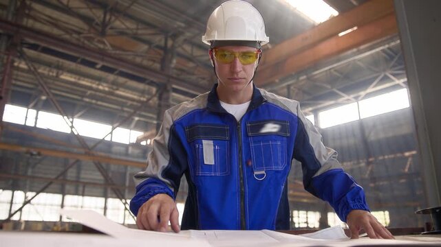 Industrial engineer in uniform use project blueprints on industry factory background, heavy manufacturing or shipyard. - Powered by Adobe