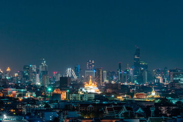 Fototapeta premium Vibrant city skyline at night featuring glowing skyscrapers, traditional architecture, and bright lights against a dark blue sky.