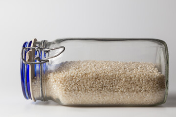 Half a glass jar of raw rice, lying on a white surface. Elements of a traditional kitchen