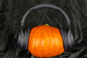 An orange autumn pumpkin wearing modern wireless headphones and listening to music, a creative still life on a dark background concept of music, podcast, audio