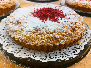  Fresh homemade crumble pie decorated with powdered sugar and dried raspberries, close-up on a wooden table. Traditional dessert for coffee shop, bakery, or homemade cuisine.