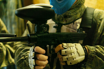 a close up shot of a man in camouflage jacket and blue mask holding a paintball gun during a game, concept of entertainment, extreme sport, hobby, games, team building.