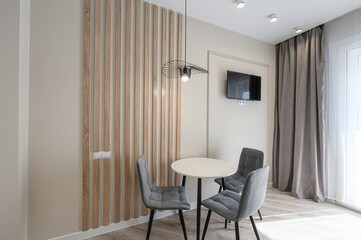 A modern interior with a small round table surrounded by three gray chairs, illuminated by a unique pendant light