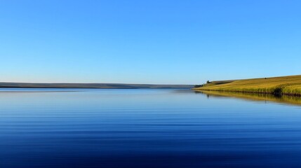 Fototapeta premium A serene lake with calm, glass-like water reflects the clear blue sky, showing gentle ripples and mirror effects,