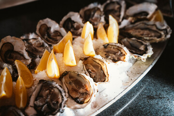 Fresh oysters served on ice with lemon wedges on a platter. The image captures the seafood's freshness, ready for dining, highlighting the contrast between the shells and citrus garnish.