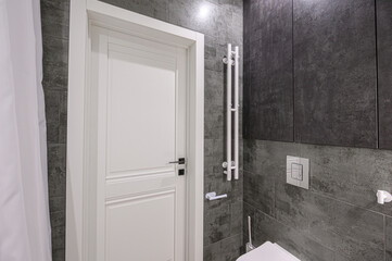 A modern bathroom featuring gray tiled walls, a white door, and minimalist fixtures. The clean lines and neutral color palette create a sleek and contemporary space