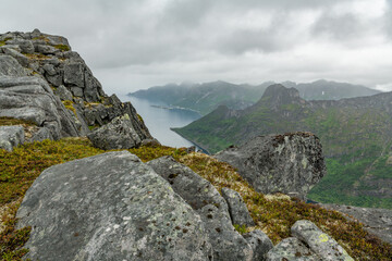 Mountains on Norwegian senja island. View from hiking trail towards Øyfjorden Barden mountain peak into the fjord. Arctic travel destination in northern europe. Amazing wilderness. Husoy in distance.